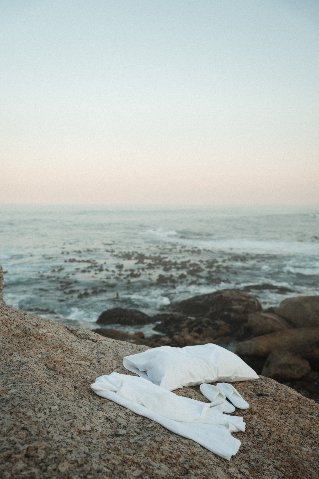 Dover pillow, robe, and slippers arranged on a coastal rock