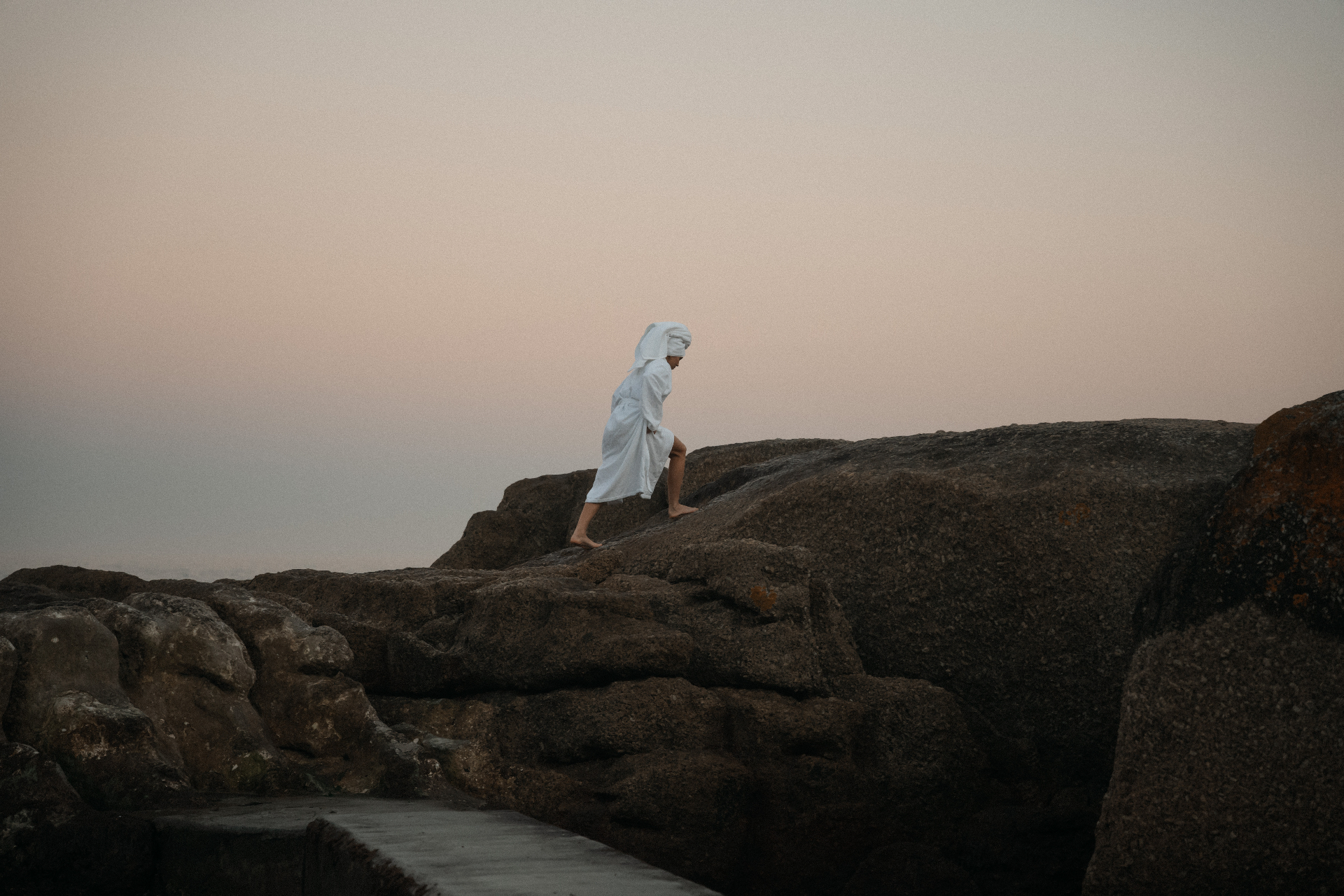 Person in a white Dover robe walking across coastal rocks at dusk