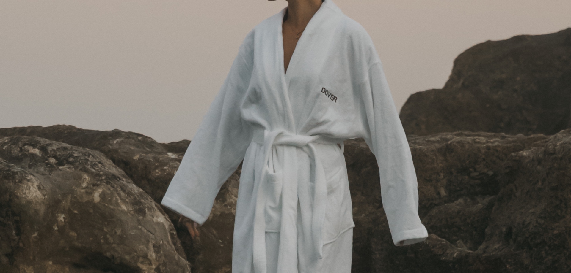 Full-length view of a white Dover robe worn amongst coastal rocks