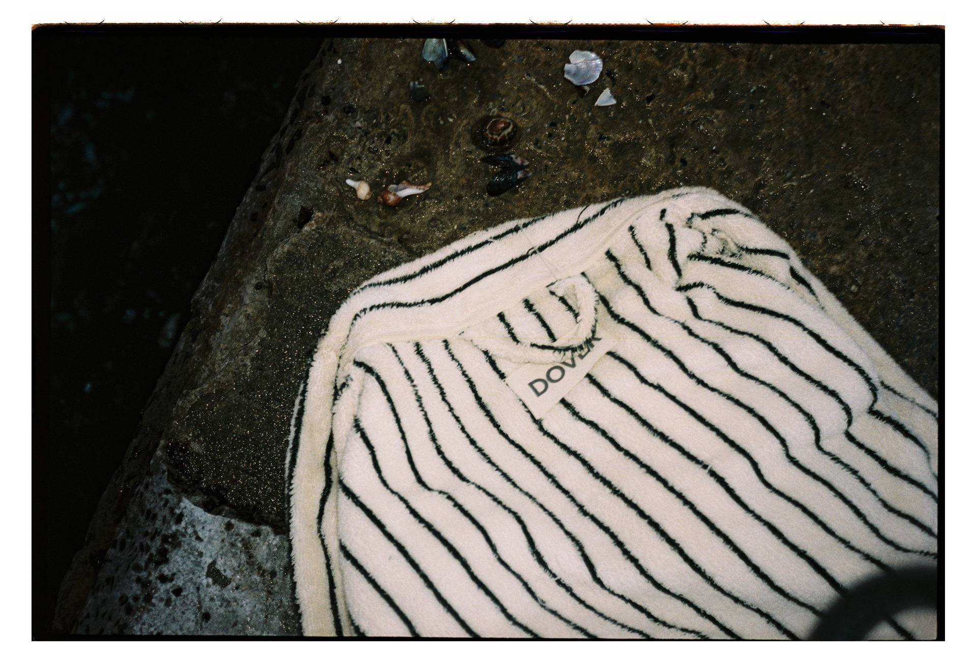 Striped Dover robe with DOVER tag laid on a coastal rock with seashells