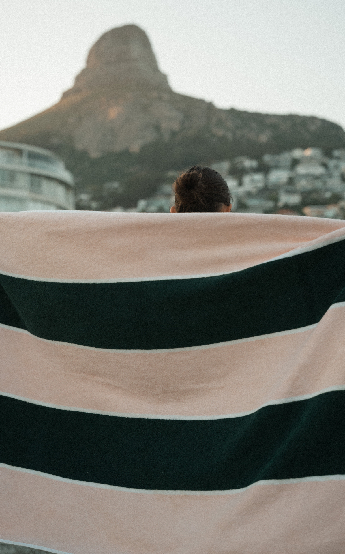 Pink and green striped Dover pool towel held up against the mountain