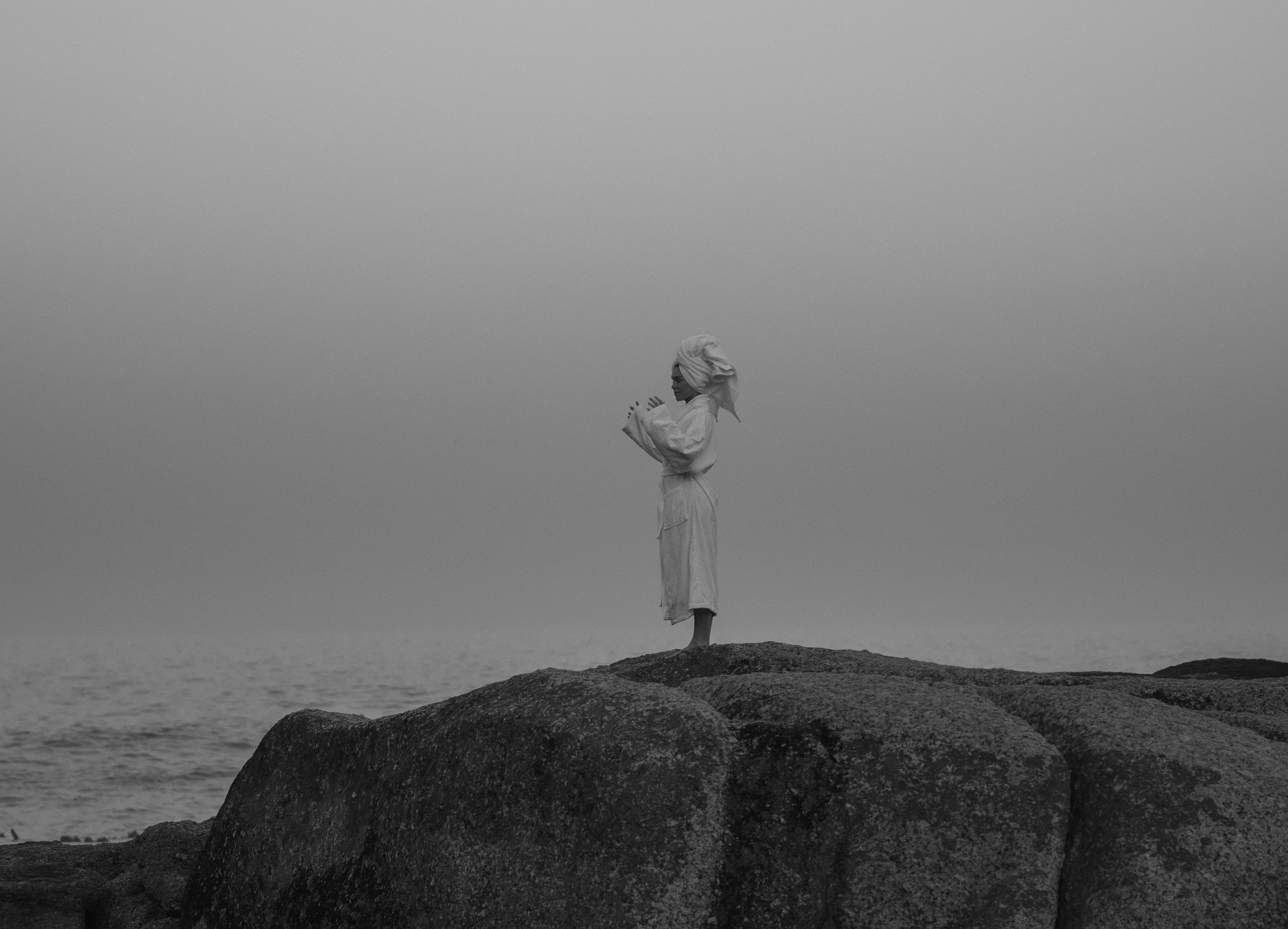 Person in a white Dover robe standing on coastal rocks by the sea